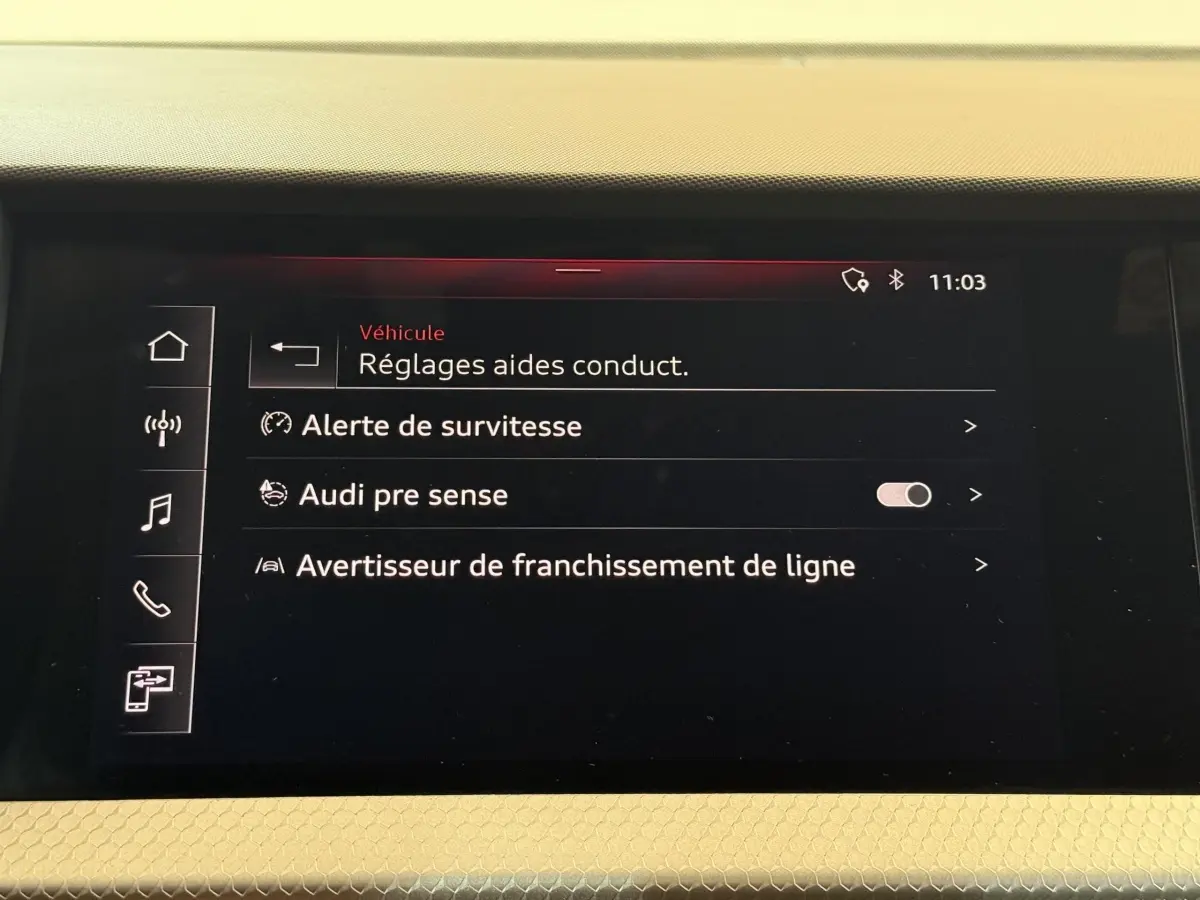 Écran tactile intérieur de l'Audi A1 2020 affichant les réglages d'aides à la conduite sur fond noir.