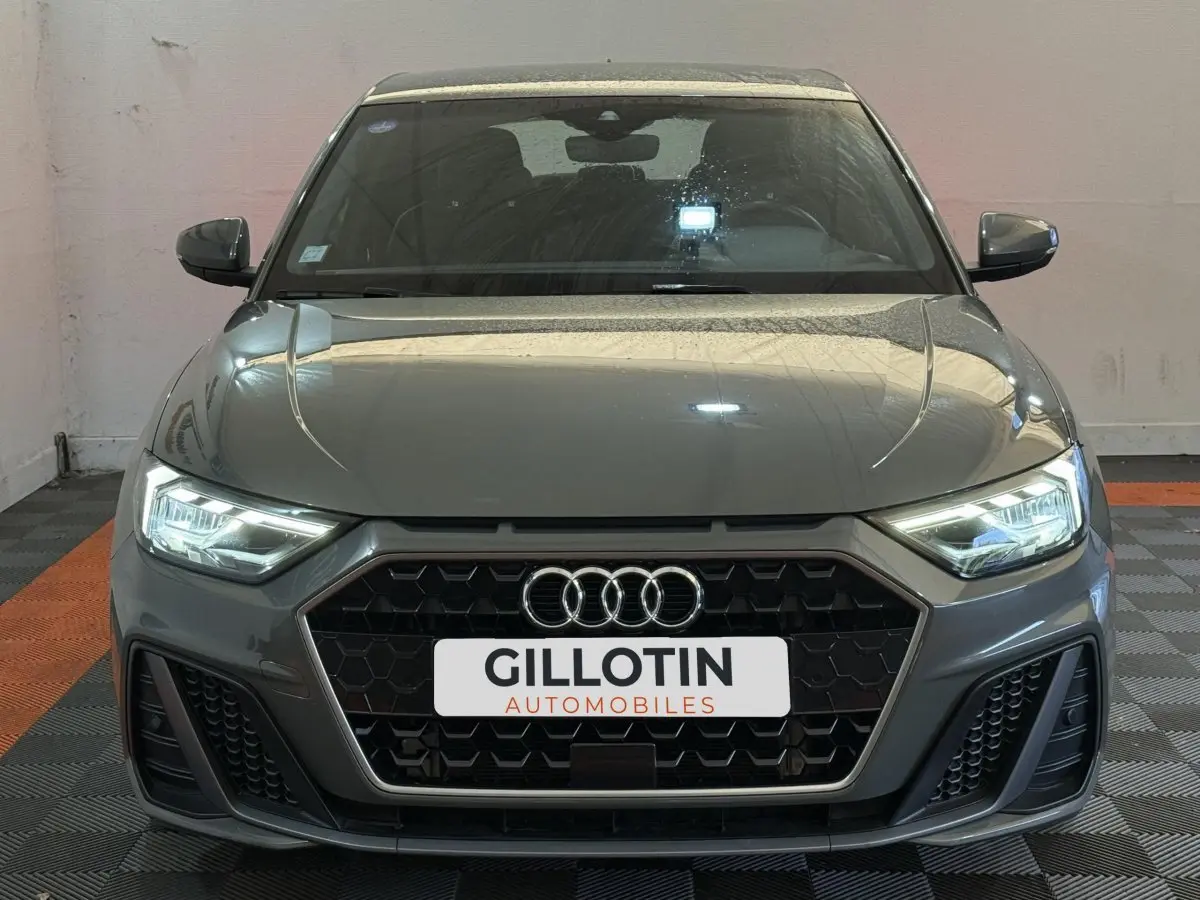 Vue frontale d'une Audi A1 S line gris foncé avec phares LED allumés et calandre hexagonale noire.