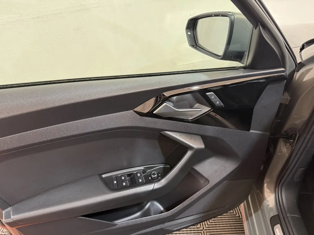 Vue intérieure du panneau de porte côté conducteur gris foncé de l'Audi A1 1.5 TFSI S line avec commandes de vitres et rétroviseur.