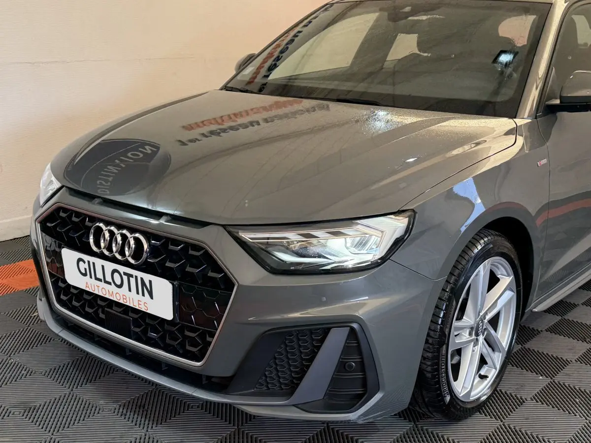 Vue 3/4 avant droit d'une Audi A1 S line gris foncé avec calandre hexagonale et phares LED allumés.