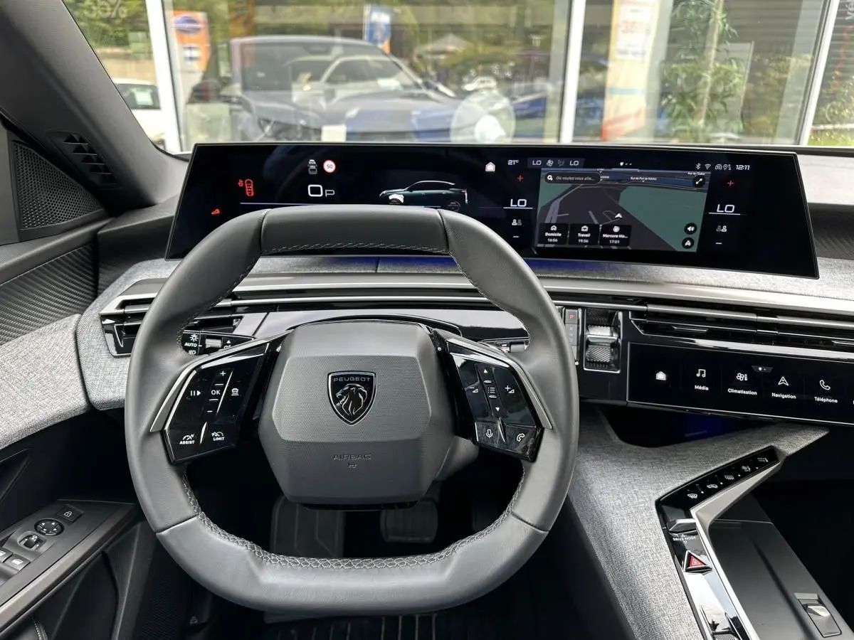 Vue intérieure centrée sur le volant cuir et le tableau de bord numérique panoramique du Peugeot 3008 gris Artense.