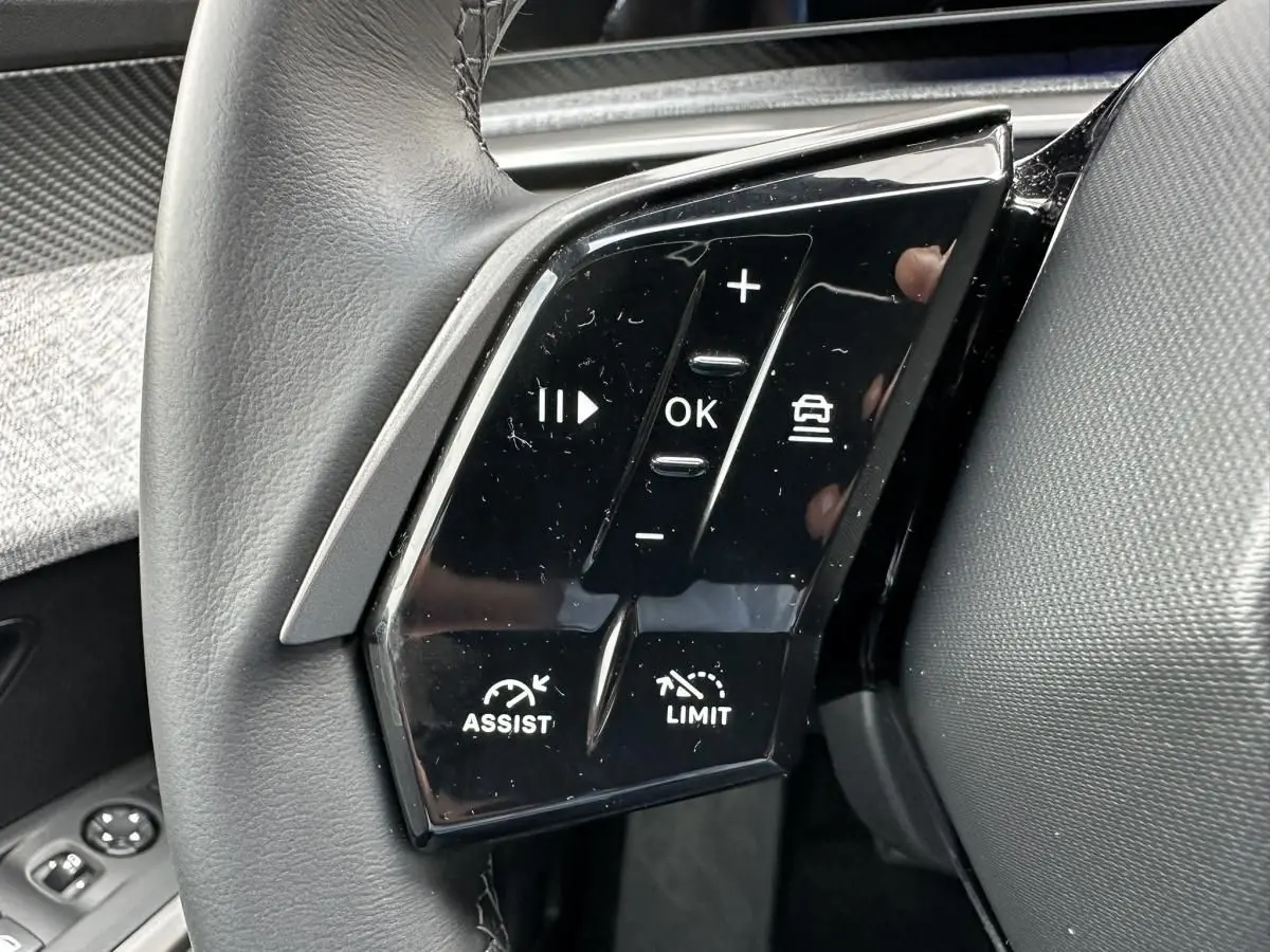 Gros plan sur les commandes au volant gauche du Peugeot 3008 2024, boutons noirs brillants avec fonctions assist et limiteur.