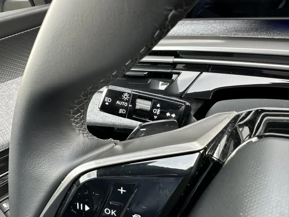 Gros plan sur le volant et la commande des phares du Peugeot 3008 2024, intérieur noir avec finitions brillantes.