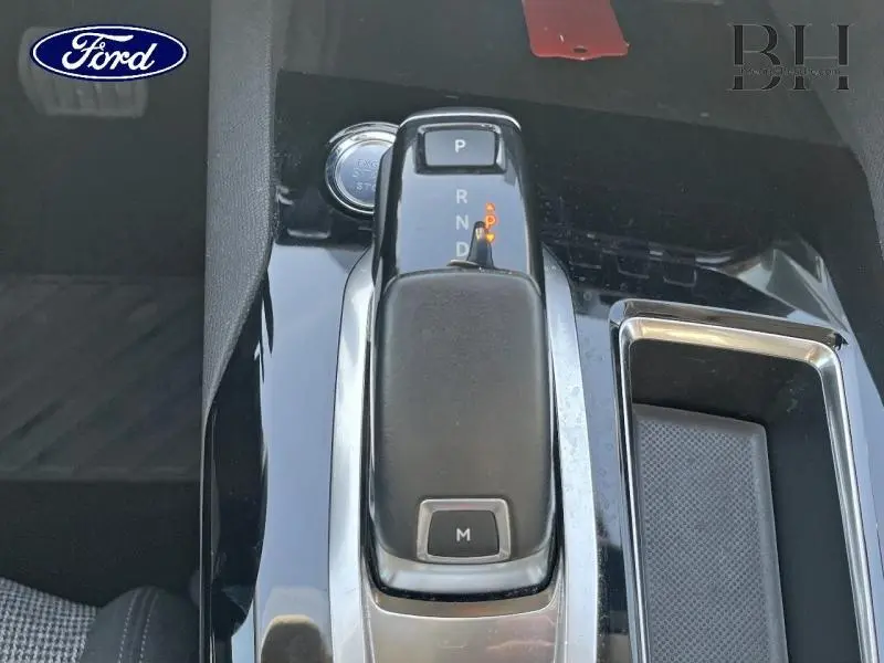 Gros plan sur la commande de boîte automatique noire et chrome dans l'habitacle, avec bouton de démarrage visible.