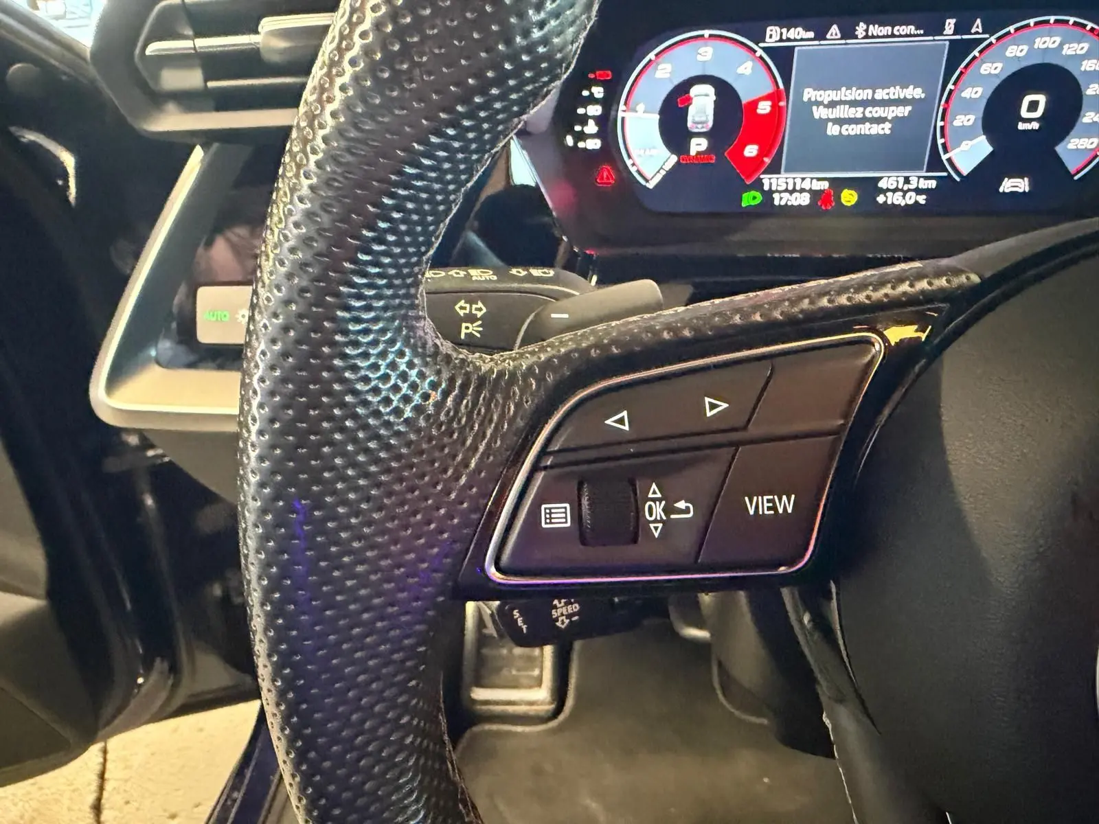 Gros plan sur le volant noir perforé et le tableau de bord numérique d’une Audi A3 bleu, version 2.0 TDI 150 S-TRONIC S-LINE.