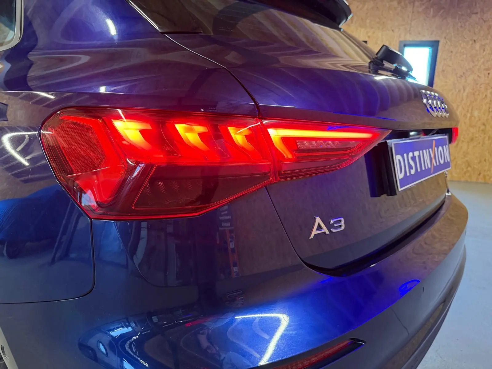 Vue 3/4 arrière droite d'une Audi A3 bleu 2022 avec feux arrière LED allumés et logo A3 visible sur le hayon.