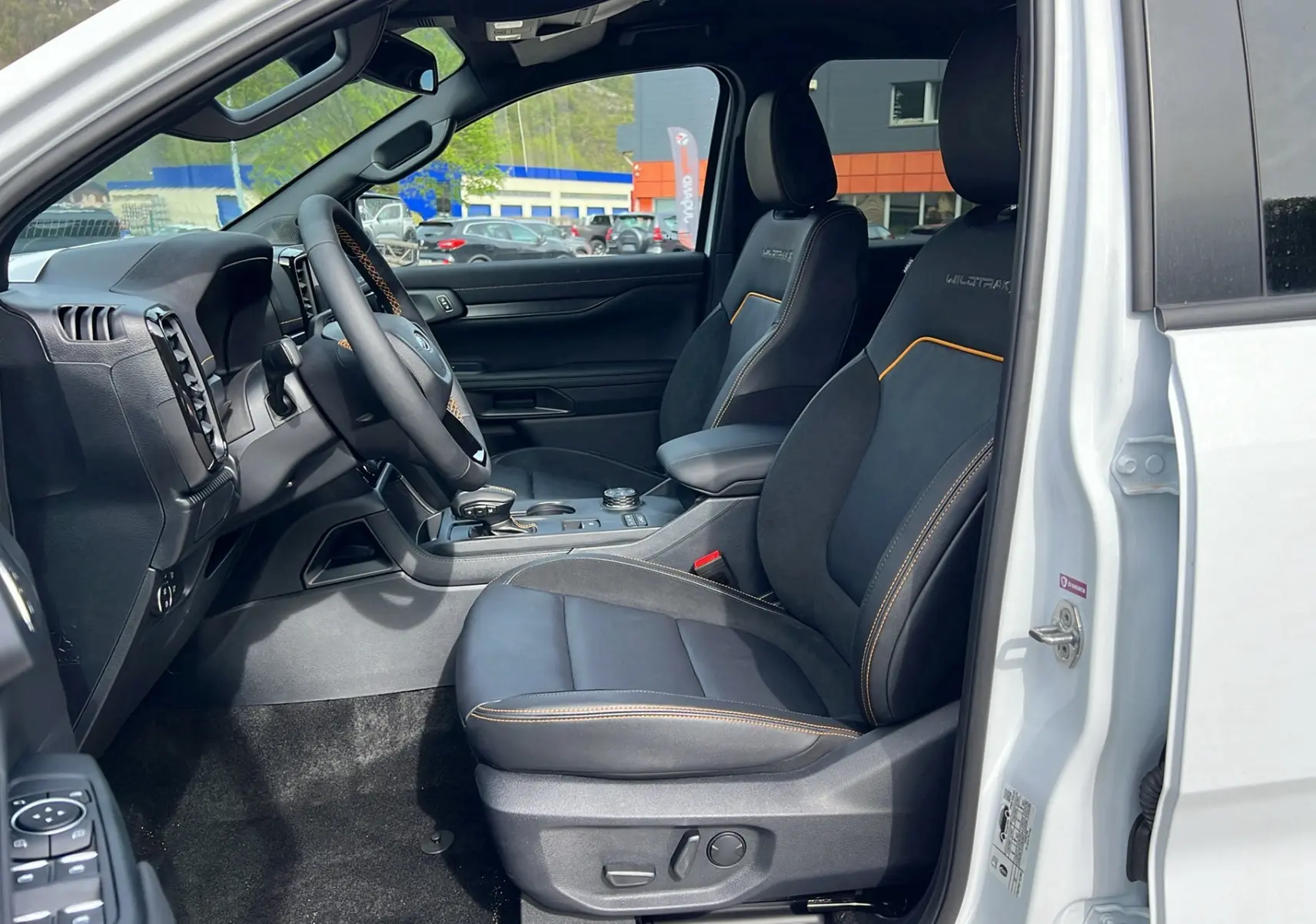 Vue intérieure côté conducteur du Ford Ranger blanc glacier 2025, sièges Wildtrak noirs avec surpiqûres orange et console centrale.