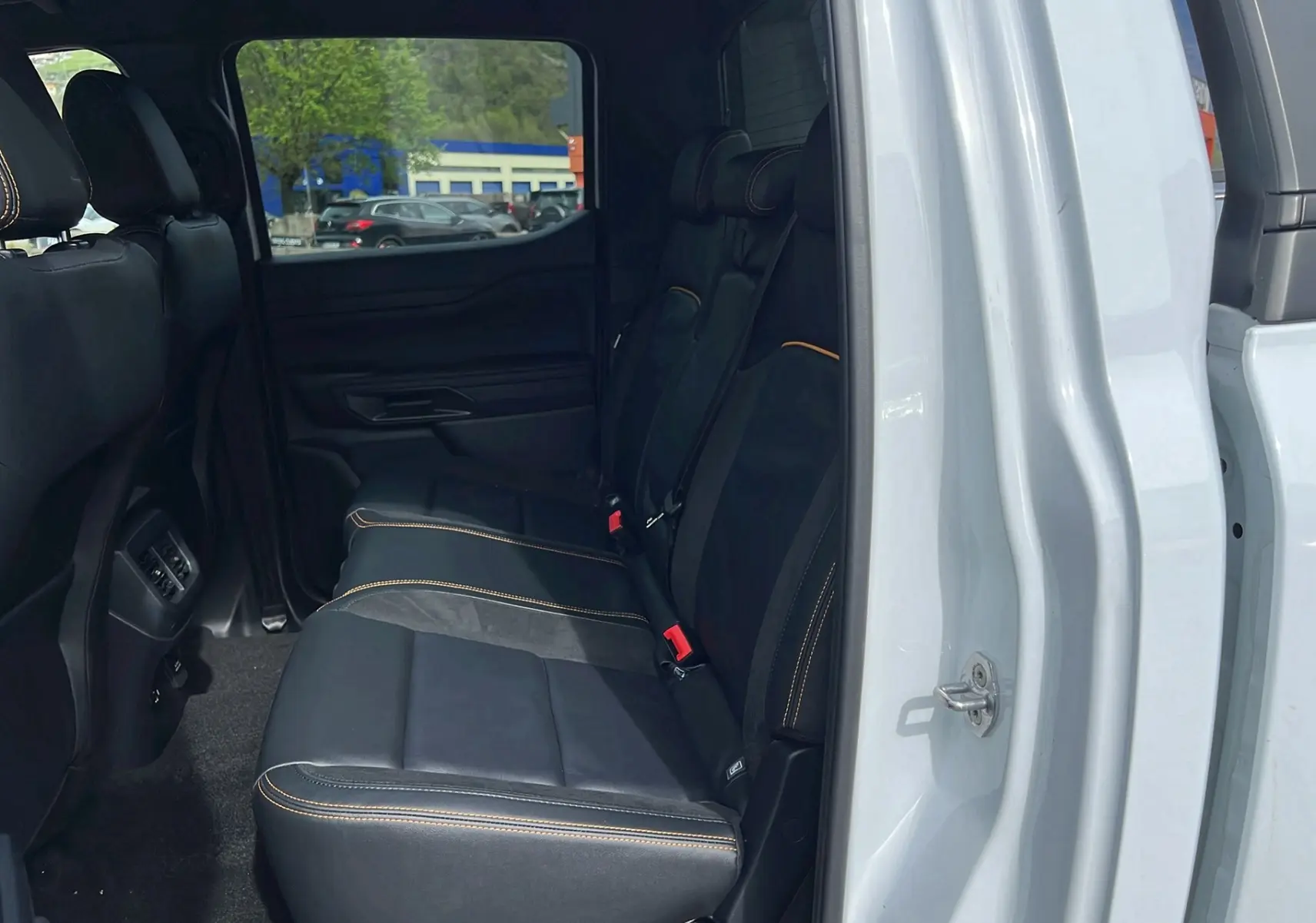 Vue intérieure côté gauche sur la banquette arrière cuir noir avec surpiqûres orange du Ford Ranger blanc glacier 2025.