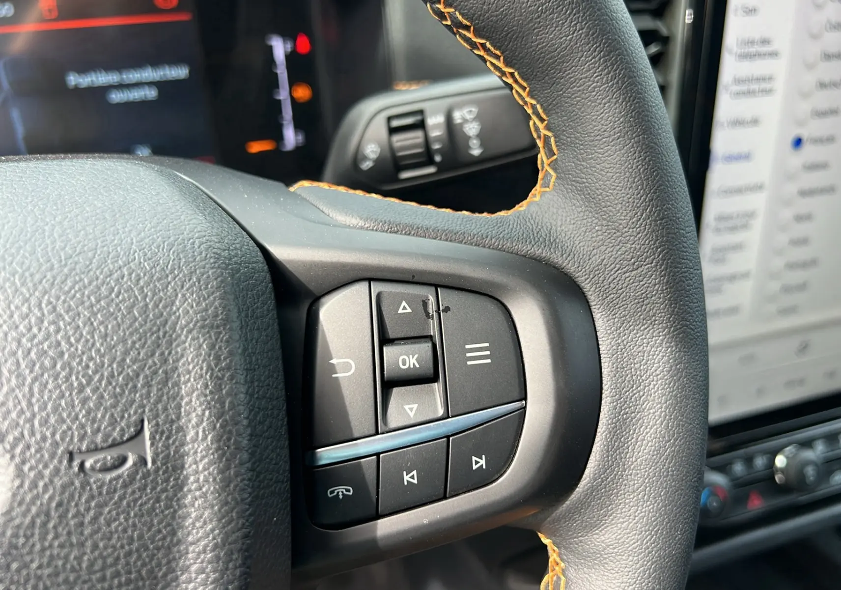 Gros plan sur les commandes multifonctions à droite du volant cuir noir avec surpiqûres orange du Ford Ranger Wildtrak 2025.