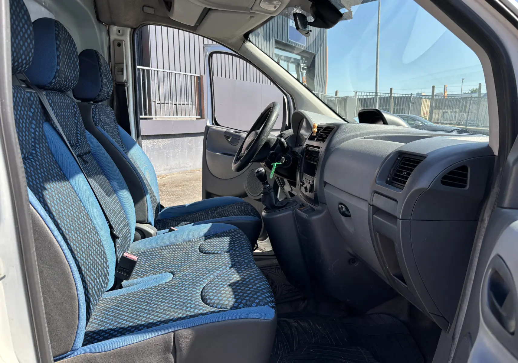 Intérieur du FIAT Scudo Fourgon 2010 vu côté gauche, sièges bleus à motifs et tableau de bord gris simple.