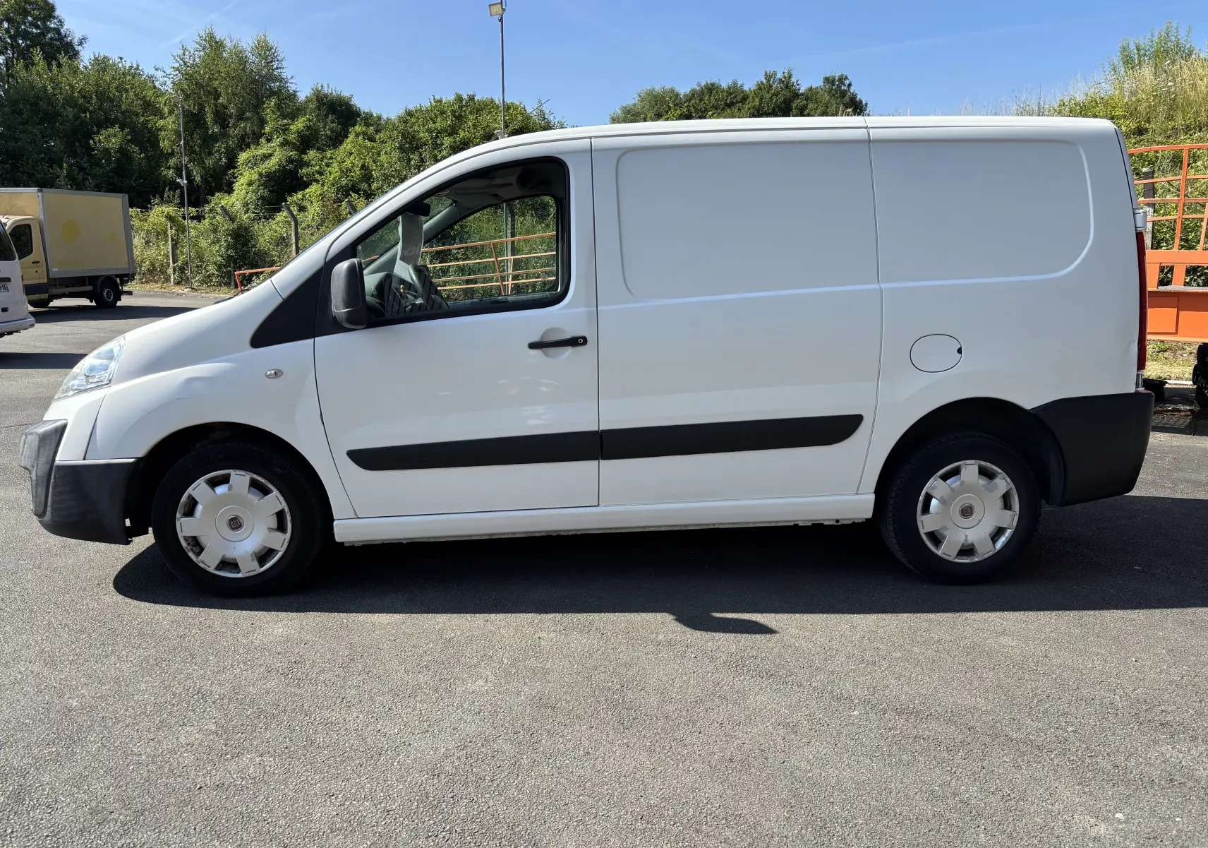 Fourgon blanc Fiat Scudo II 1.6 MJTD vu de profil côté gauche, avec bande noire latérale et jantes d'origine.