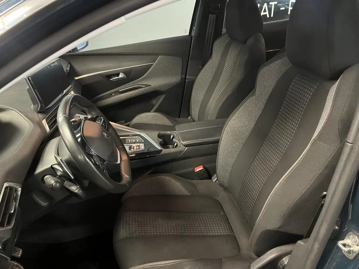 Intérieur côté conducteur du Peugeot 3008 bleu 2022, sièges textile gris et volant cuir compact multi-fonctions.