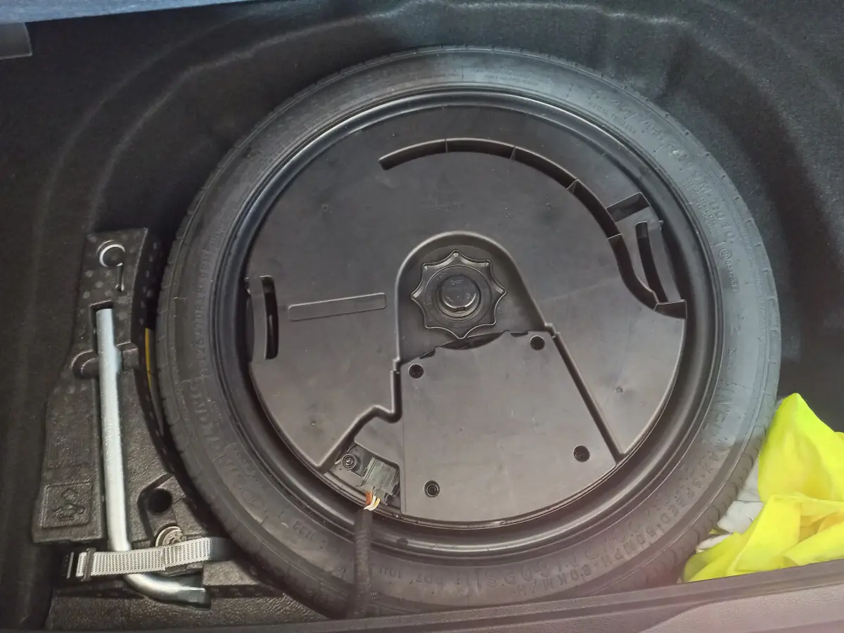 Gros plan sur la roue galette de secours dans le coffre d'une Volkswagen Golf bleue 2022, avec outil de levage visible.