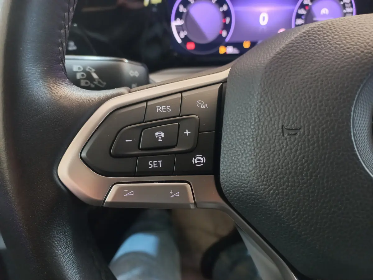 Gros plan sur les commandes du volant côté gauche de la Volkswagen Golf 1.5 bleu, avec tableau de bord numérique en arrière-plan.