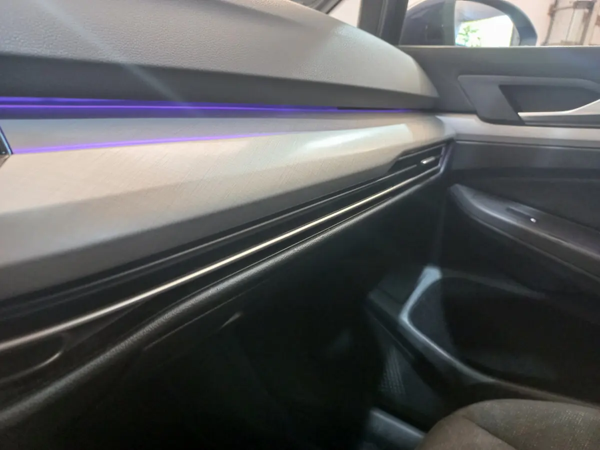 Détail du tableau de bord côté passager avec éclairage d'ambiance violet dans une Volkswagen Golf bleue 2022.