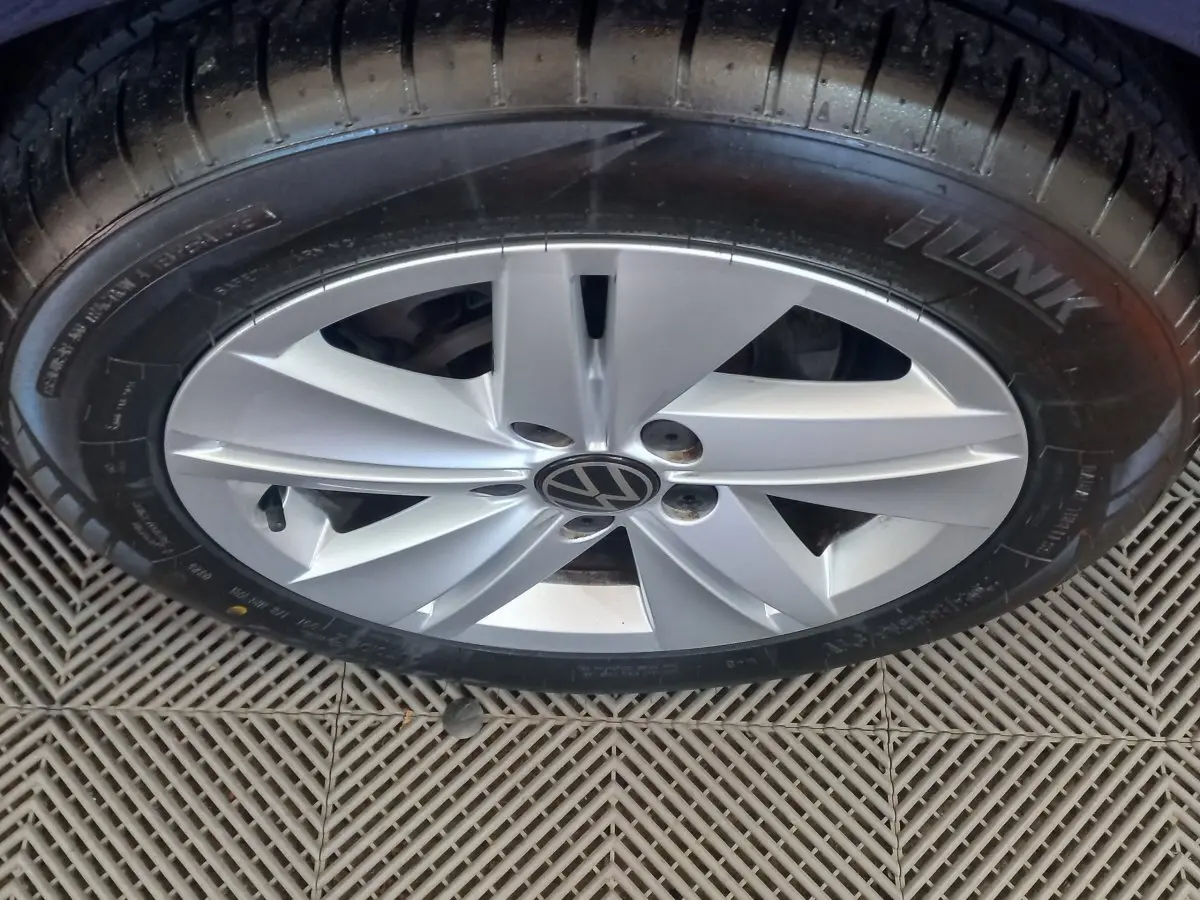 Gros plan sur la jante argentée avec logo Volkswagen d'une Golf bleue, vue du dessus sur sol carrelé.