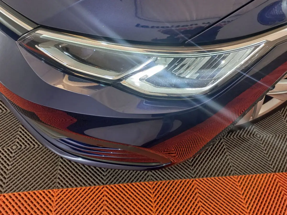 Gros plan sur le phare avant droit d'une Volkswagen Golf bleu profond avec reflets sur la carrosserie