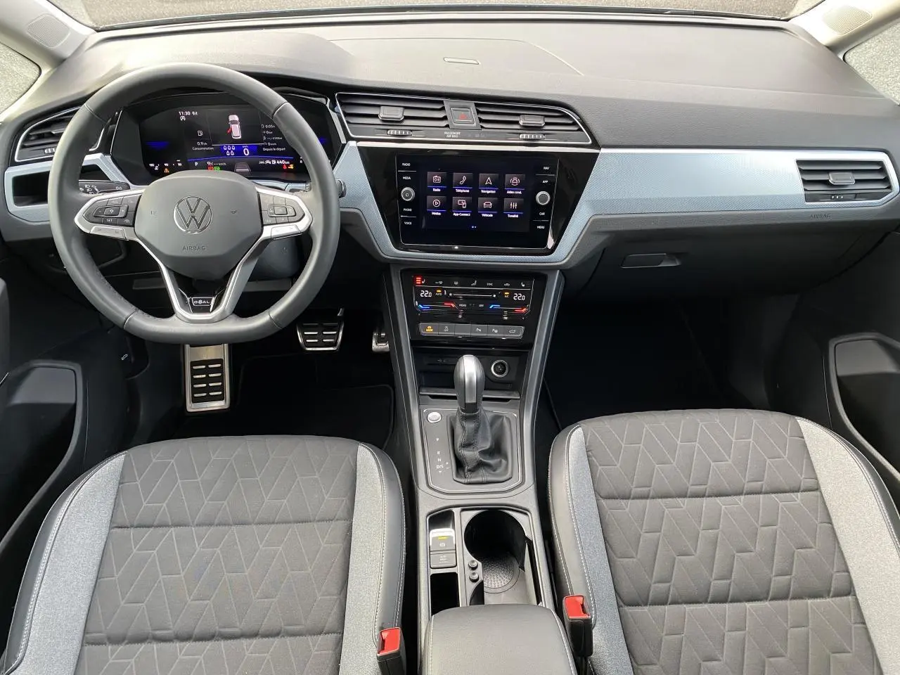 Vue intérieure frontale du tableau de bord et volant Volkswagen Touran 2025 avec sellerie grise et écran tactile central.