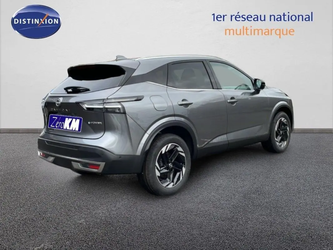 Vue 3/4 arrière droit d'un Nissan Qashqai gris 2025 avec jantes aluminium et barres de toit visibles.