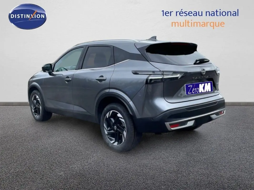 Vue 3/4 arrière droite d'un Nissan Qashqai gris 2025 avec jantes aluminium et barres de toit visibles.