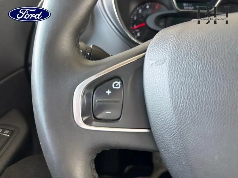 Gros plan sur le volant gris avec commandes de régulateur de vitesse, intérieur sombre, détails du tableau de bord flous.