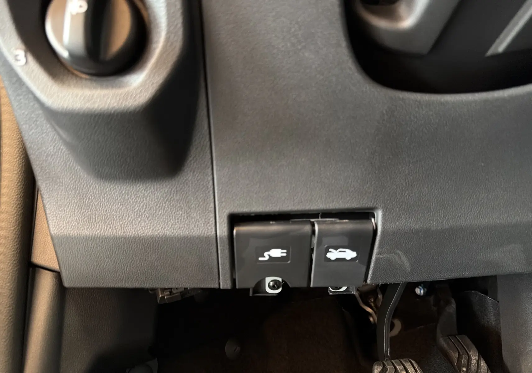 Détail intérieur montrant les commandes d'ouverture du capot et de la trappe de recharge sur Dacia Spring 65 Extreme 2026.