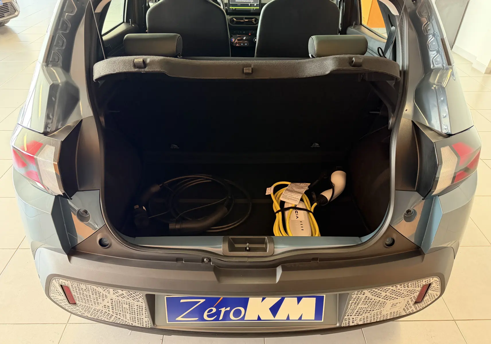 Vue arrière du Dacia Spring 65 Extreme bleu ardoise 2026 avec coffre ouvert et câbles de recharge électrique visibles.