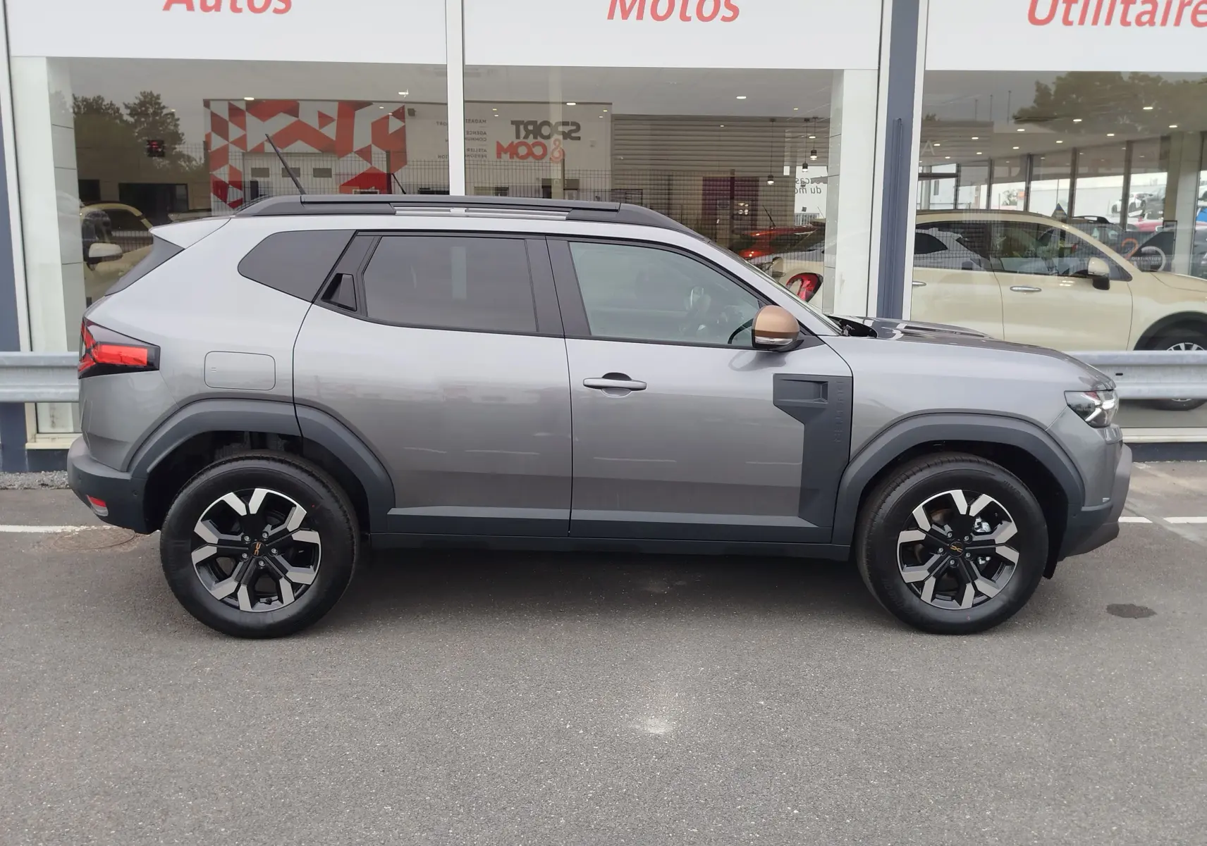 Profil côté droit du Dacia Duster 2025 gris schiste avec jantes noires et coques de rétroviseurs couleur cuivre.