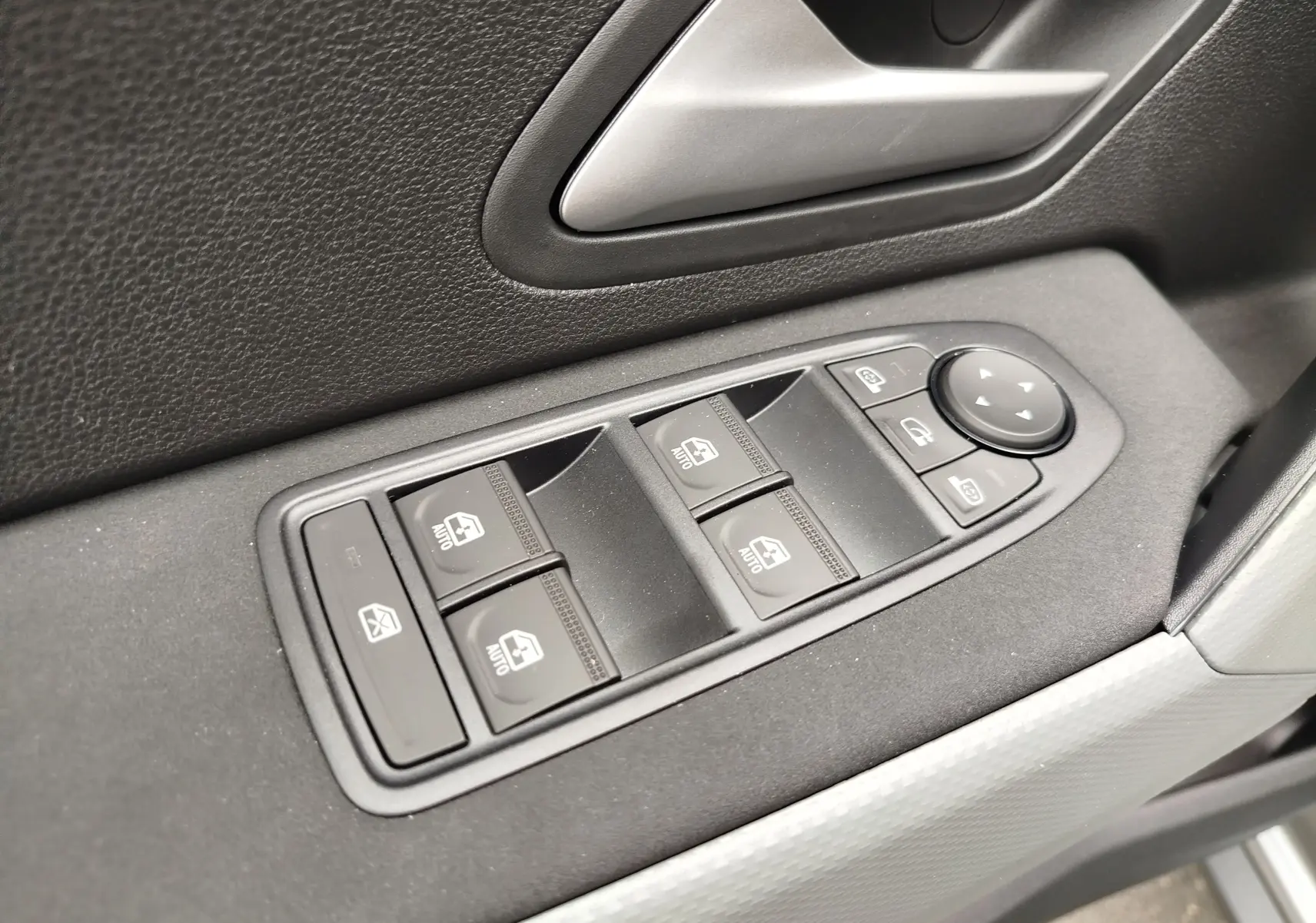 Gros plan sur les commandes des vitres électriques et rétroviseurs côté conducteur du Dacia Duster gris schiste 2025.