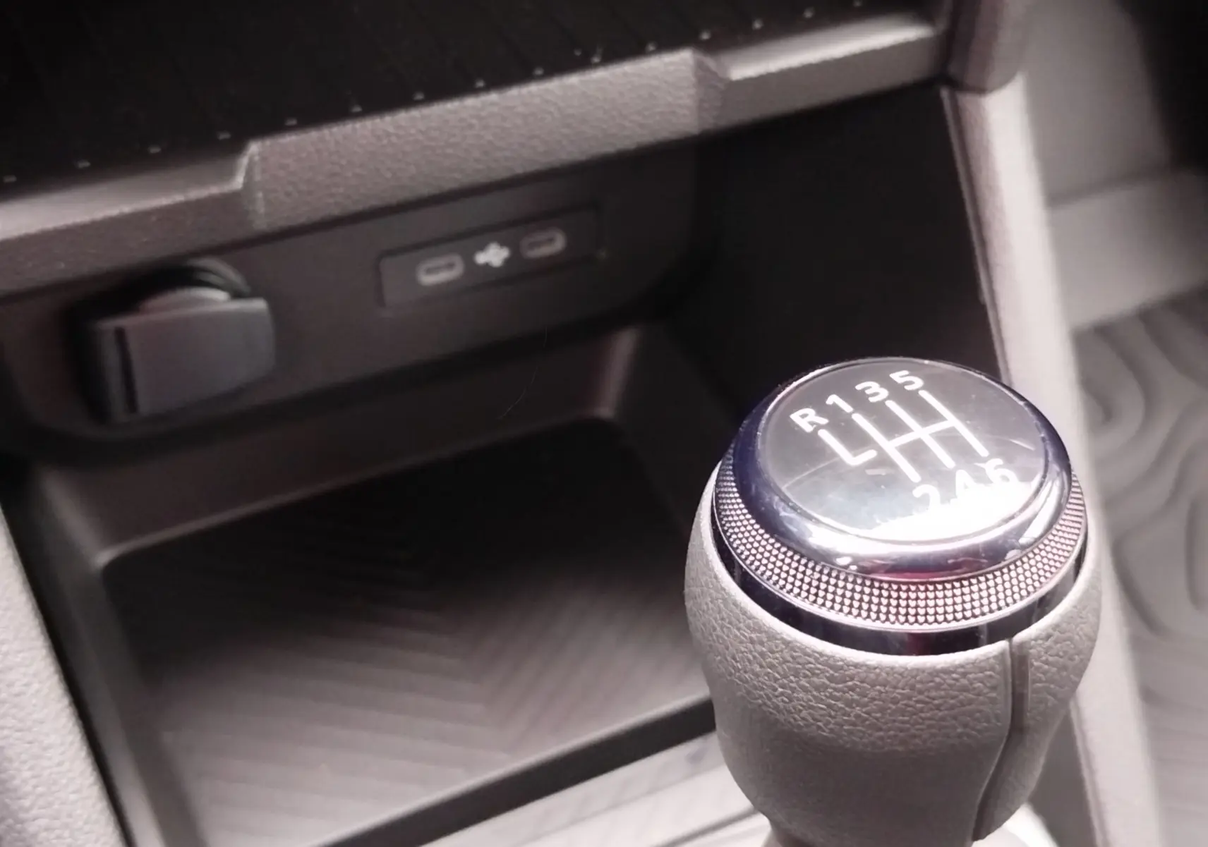 Gros plan sur le levier de vitesses manuel du Dacia Duster gris schiste, avec prise USB et rangement en arrière-plan.