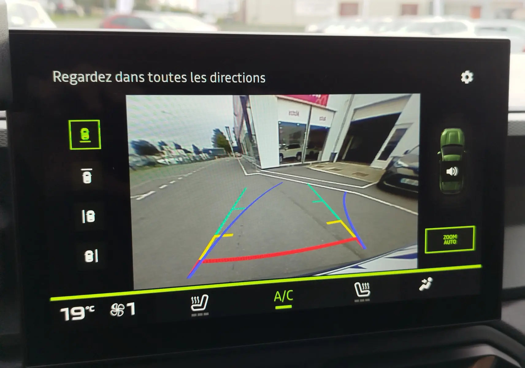 Affichage caméra de recul du Dacia Duster gris schiste, vue arrière avec lignes de guidage colorées et environnement urbain visible.