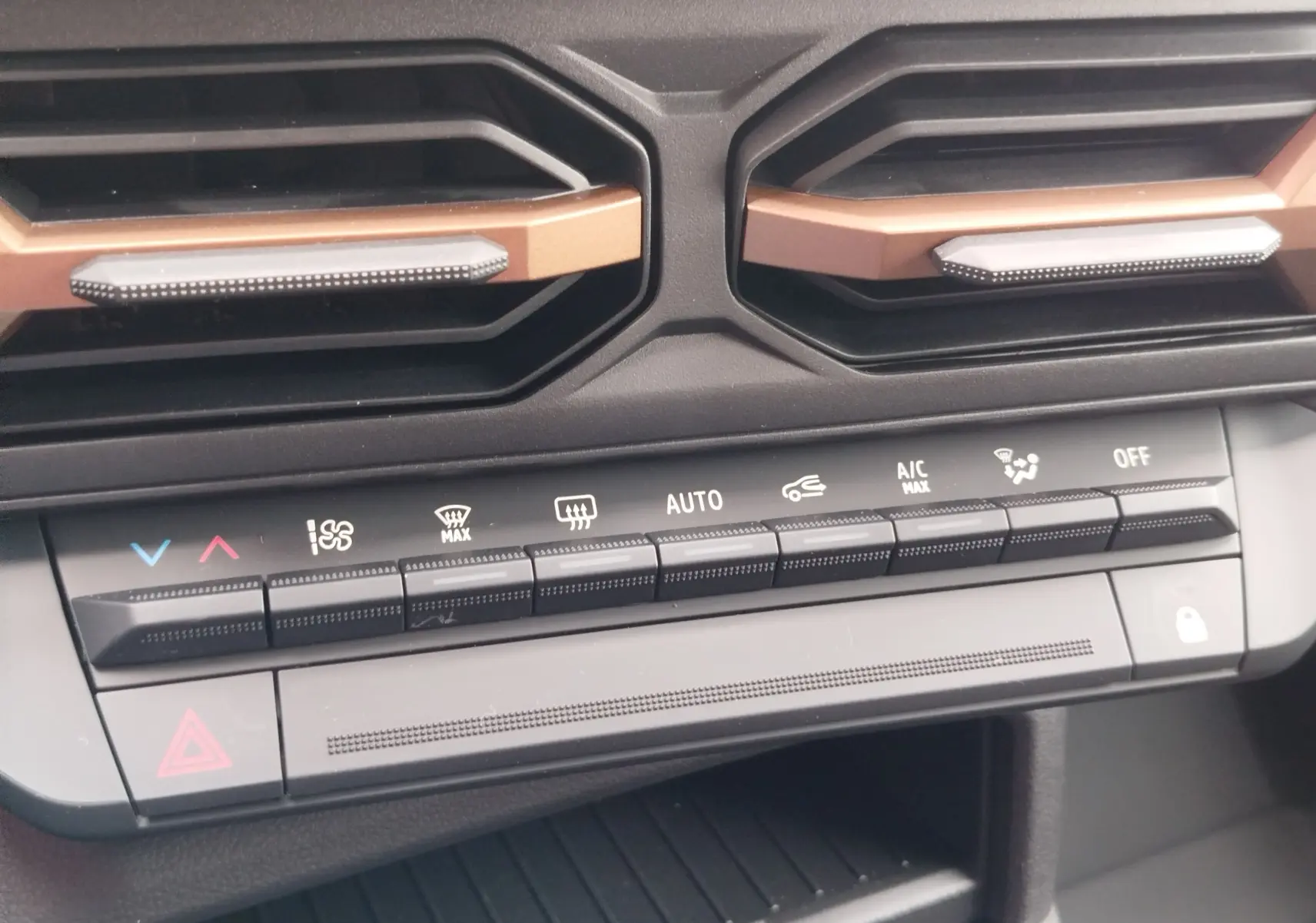Vue rapprochée des commandes de climatisation et des aérateurs noirs avec inserts cuivrés du tableau de bord du Dacia Duster gris schiste.