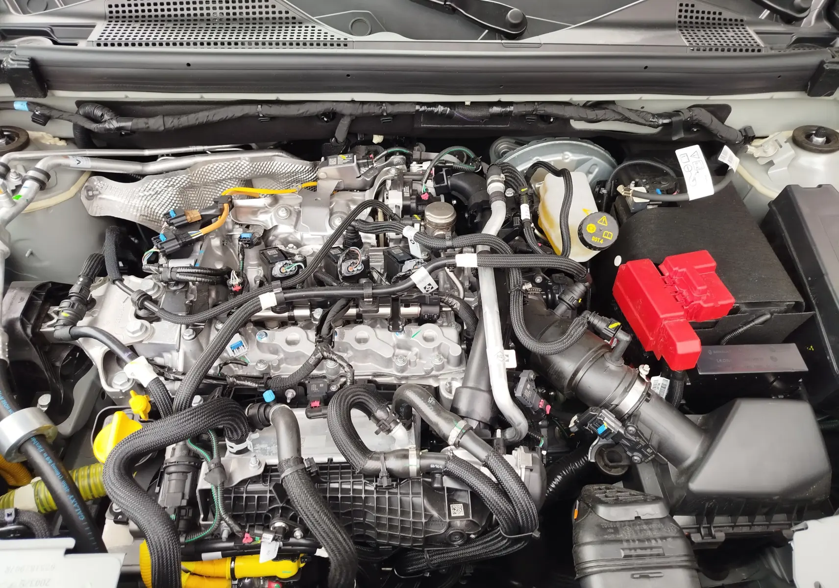 Vue rapprochée du moteur essence du Dacia Duster 2025 gris schiste, montrant câblages et batterie avec capot ouvert.