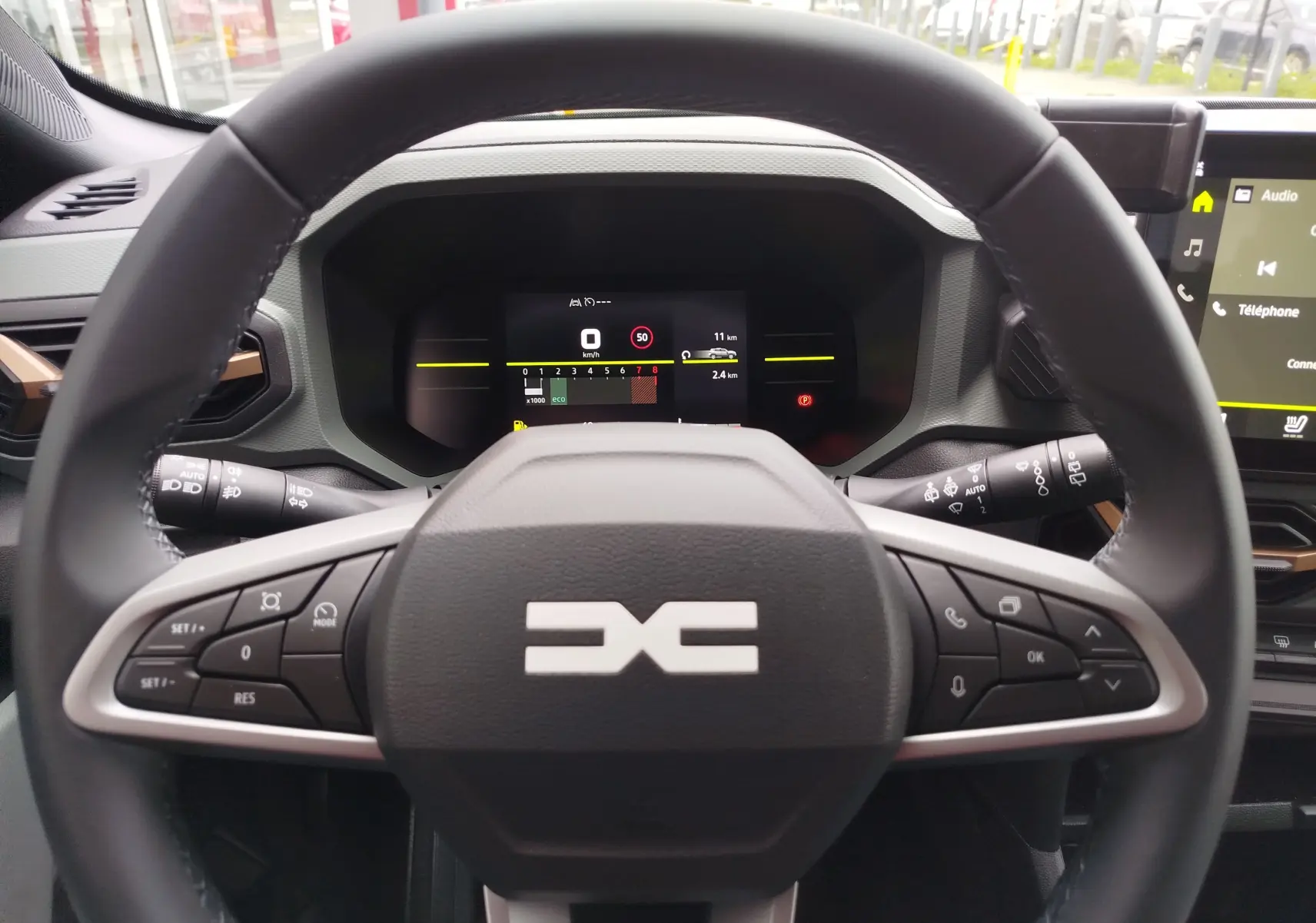 Vue centrée sur le volant noir du Dacia Duster gris schiste 2025 avec commandes intégrées et tableau de bord numérique.