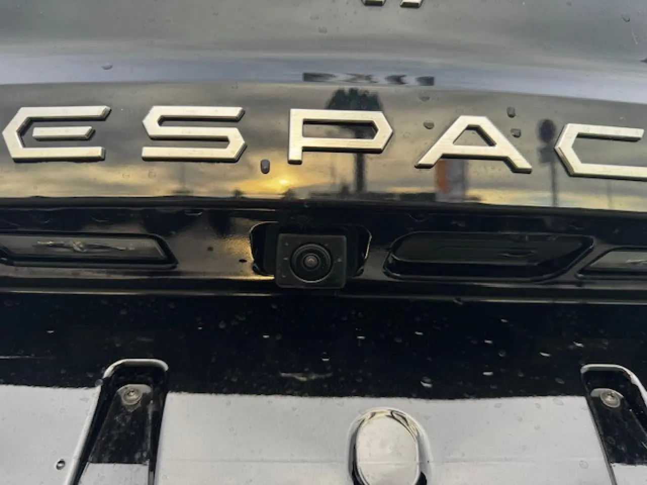 Gros plan sur la caméra de recul intégrée sous le logo ESPACE sur la malle arrière noire étoilée du Renault Espace VI.