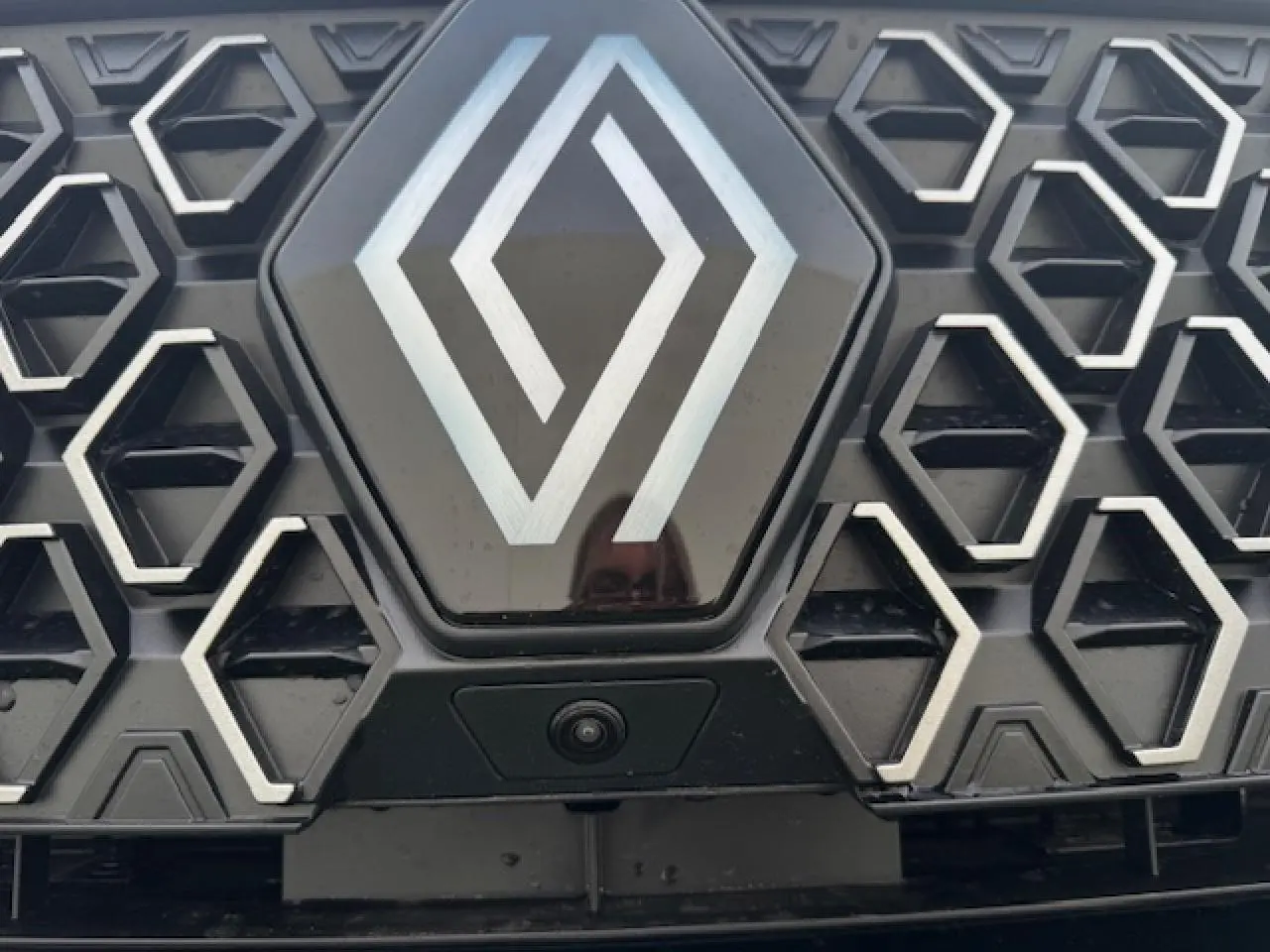 Gros plan sur la calandre noire étoilée du Renault Espace VI avec logo central et caméra avant intégrée.