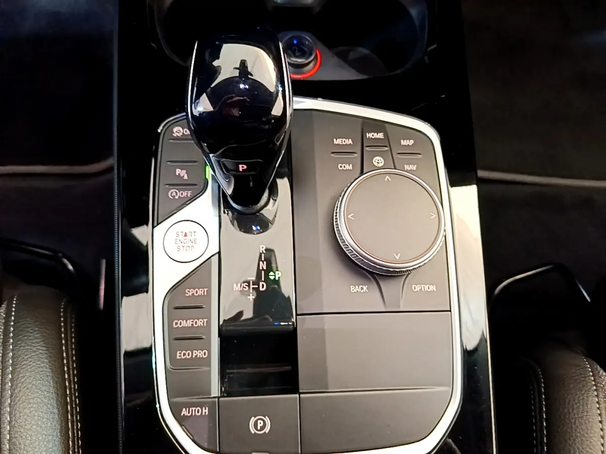 Gros plan sur la console centrale noire brillante de la BMW Série 1 118i 2021 avec levier de vitesse automatique et molette de contrôle.