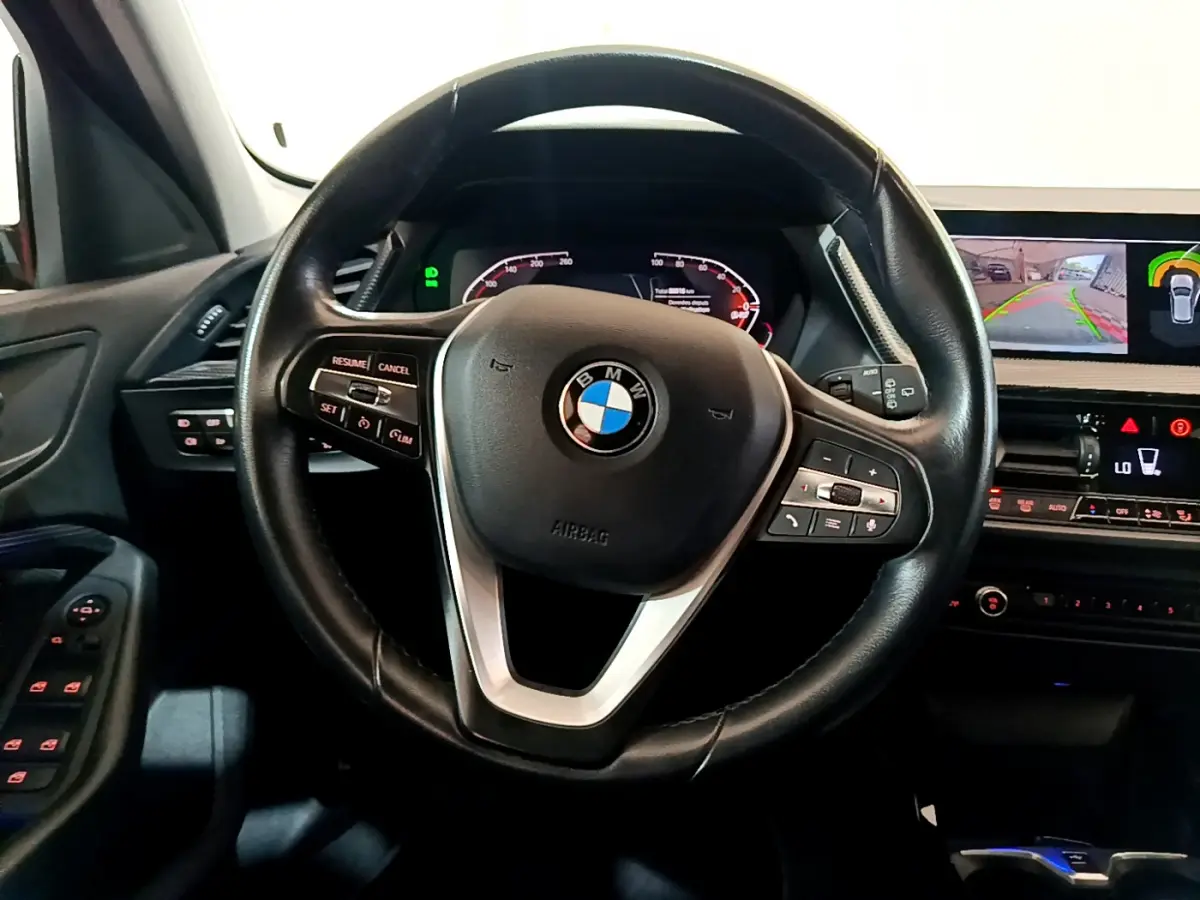 Vue rapprochée du volant cuir BMW Série 1 gris clair avec tableau de bord numérique et écran de caméra de recul.