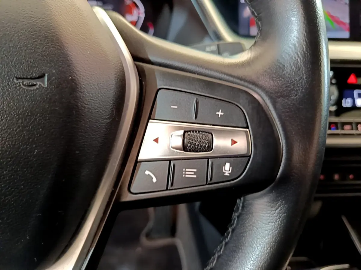 Gros plan sur les commandes du volant cuir noir de la BMW Série 1 gris clair, avec boutons multifonctions et molette argentée.