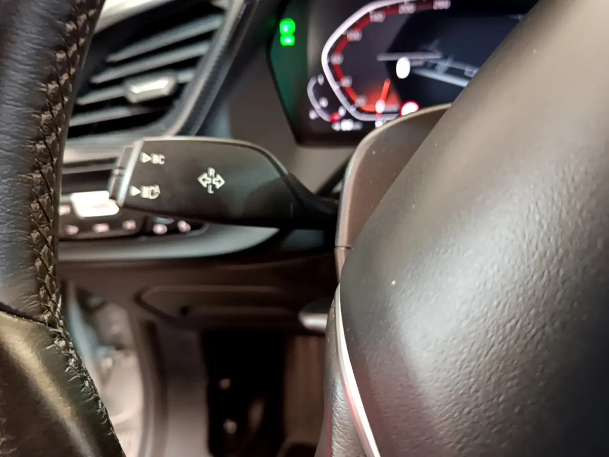 Gros plan sur le volant cuir et la commande de clignotants à gauche du tableau de bord numérique de la BMW Série 1 gris clair.