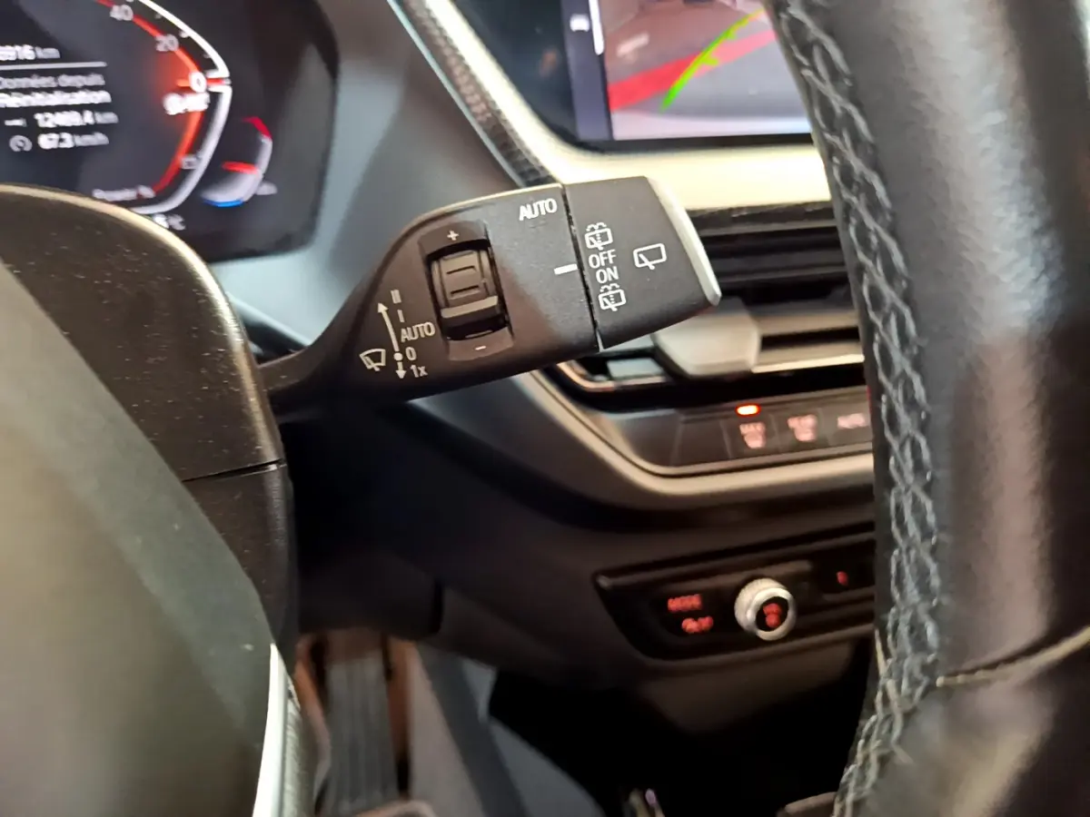 Gros plan sur la commande d'essuie-glace à gauche du volant cuir d'une BMW Série 1 gris clair, tableau de bord en arrière-plan.