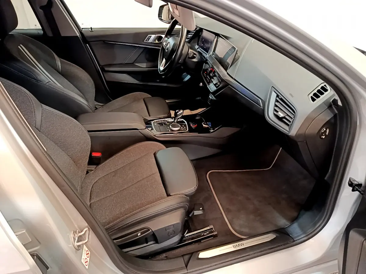 Intérieur avant droit d'une BMW Série 1 gris clair, sièges tissu et cuir, tableau de bord moderne avec écran digital.