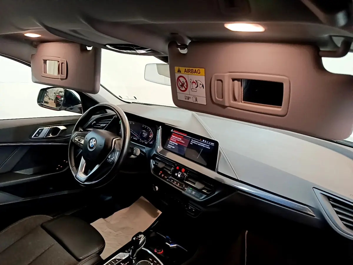 Intérieur BMW Série 1 2021 vu côté conducteur, tableau de bord noir avec écran tactile et volant cuir multifonctions.