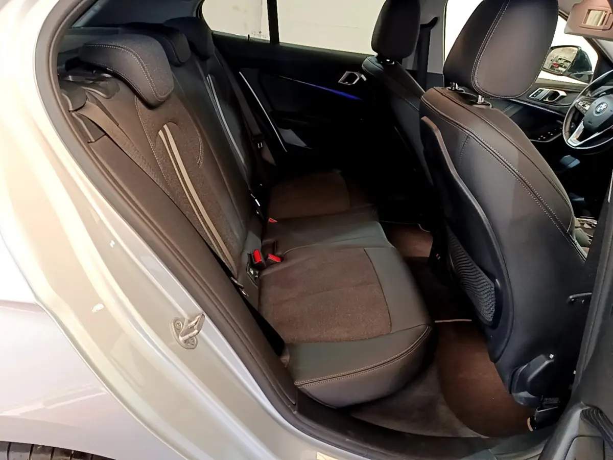 Vue intérieure côté arrière gauche de la BMW Série 1 gris clair, montrant la banquette arrière et une partie du tableau de bord.