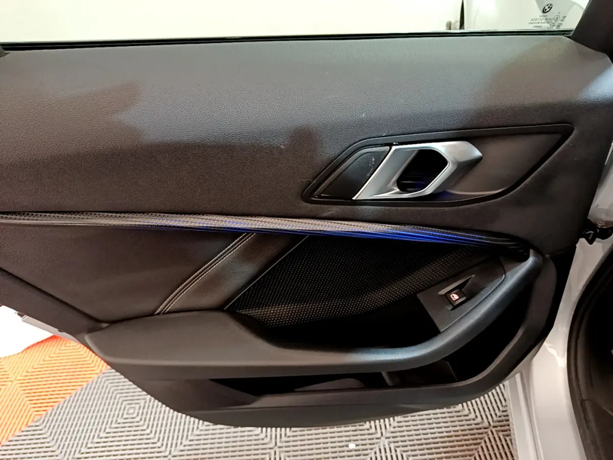 Gros plan sur la porte intérieure côté gauche d'une BMW Série 1 gris clair avec poignée alu et éclairage d'ambiance bleu