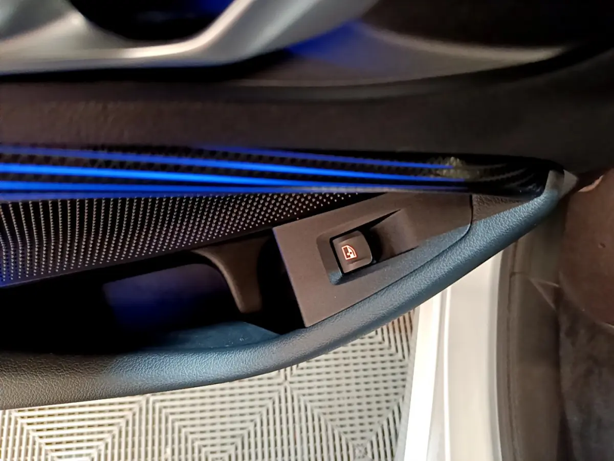 Détail de la portière côté gauche de la BMW Série 1 gris clair, avec éclairage d'ambiance bleu et bouton de verrouillage des vitres.