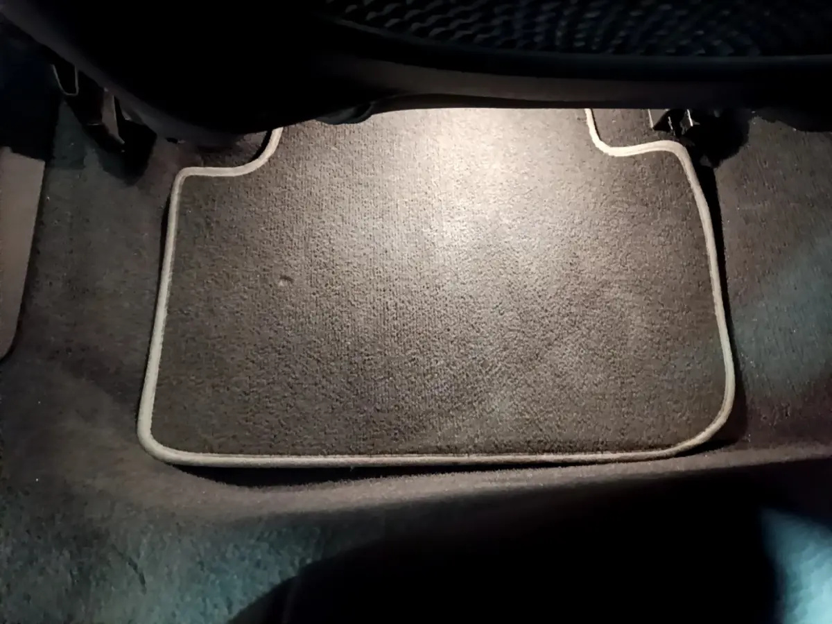 Tapis de sol gris foncé avec bordure claire, vue rapprochée de l'intérieur au niveau des pieds avant d'une BMW Série 1.