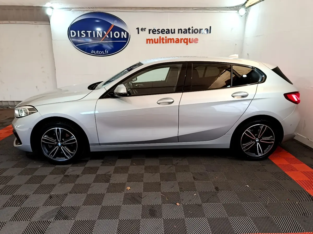 Profil côté gauche d'une BMW Série 1 gris clair 2021 Edition Sport, avec jantes alliage et feux arrière LED visibles.