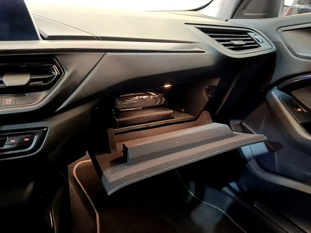 Vue intérieure côté passager du tableau de bord et boîte à gants ouverte d'une BMW Série 1 gris clair Edition Sport 2021.