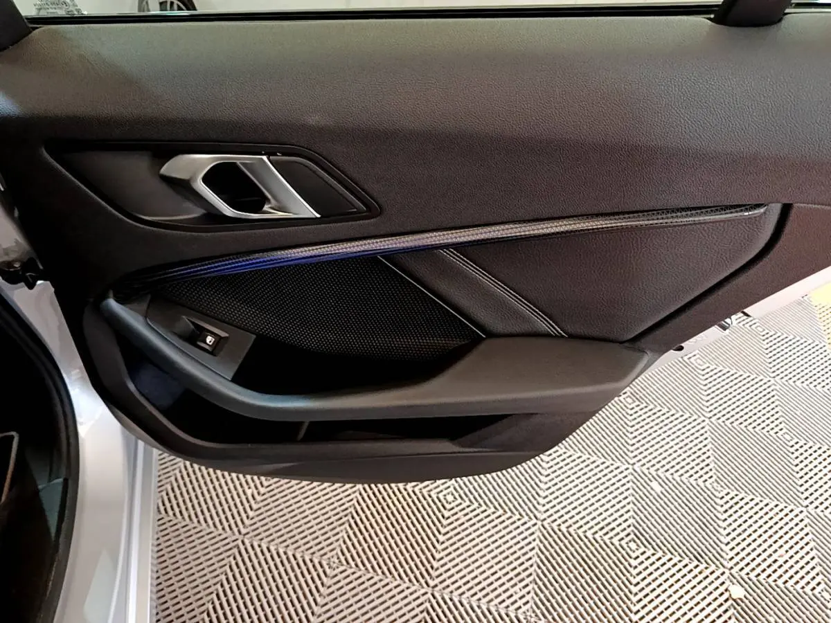 Gros plan sur la porte côté gauche d'une BMW Série 1 gris clair, mettant en valeur la poignée intérieure et les finitions noires.